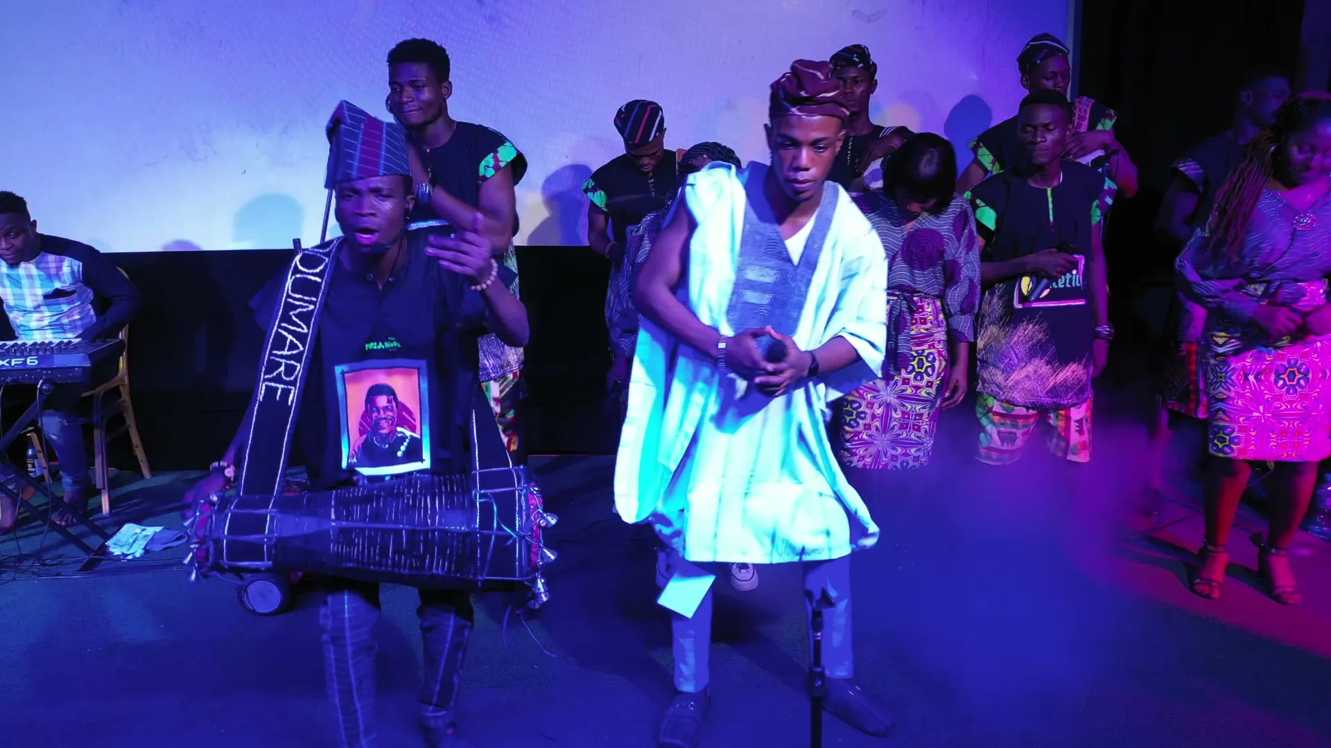 A drummer and a performer in agbada face each other, from above